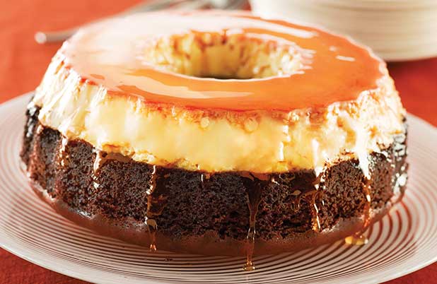 A chocolate bundt cake topped with flan on a white platter.